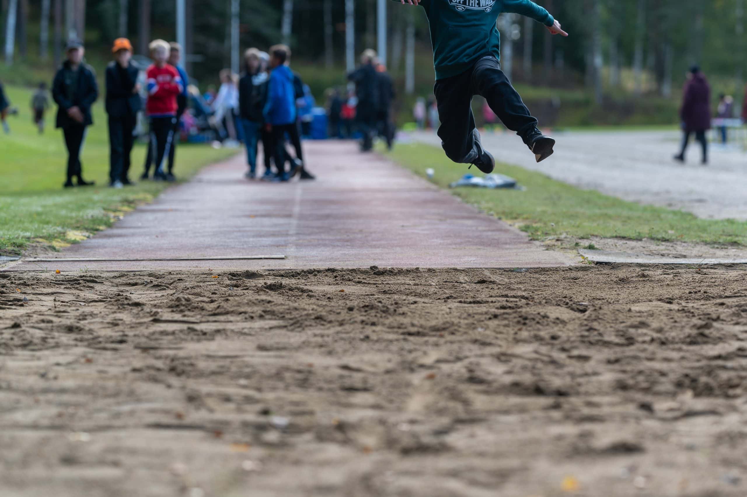Kuva urheilukilpailusta, jossa lapsi hyppää pituutta.