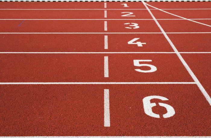 A red running track with white lane lines and numbered starting positions