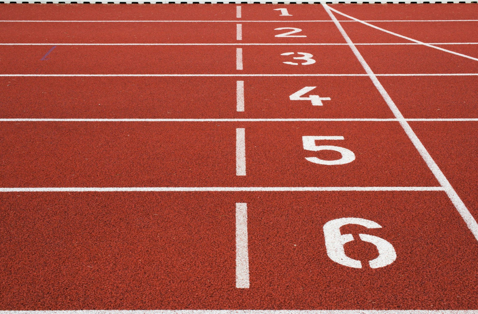 A red running track with white lane lines and numbered starting positions