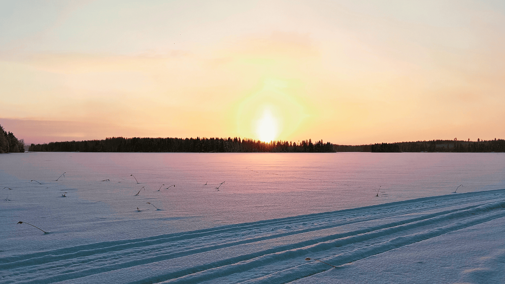 Talvinen maisema järven jäältä, jossa näkyy hiihtolatu ja auringonlasku.